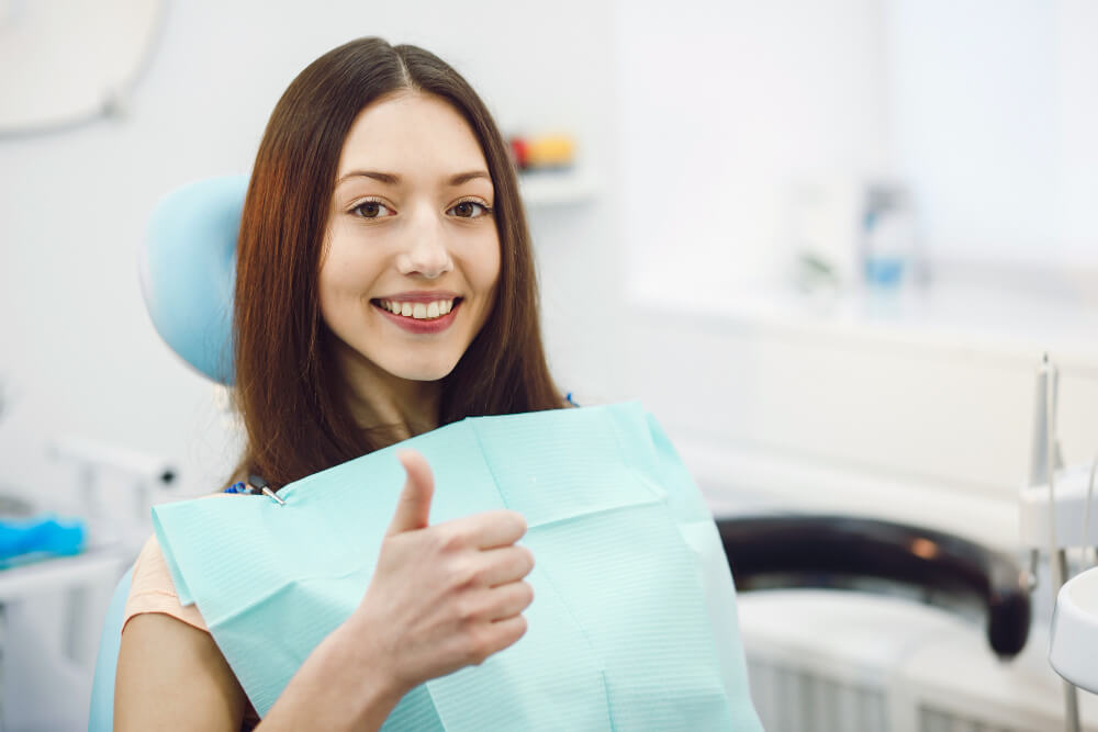 woman sitting on the dental chair smiling while holding a thumbs up