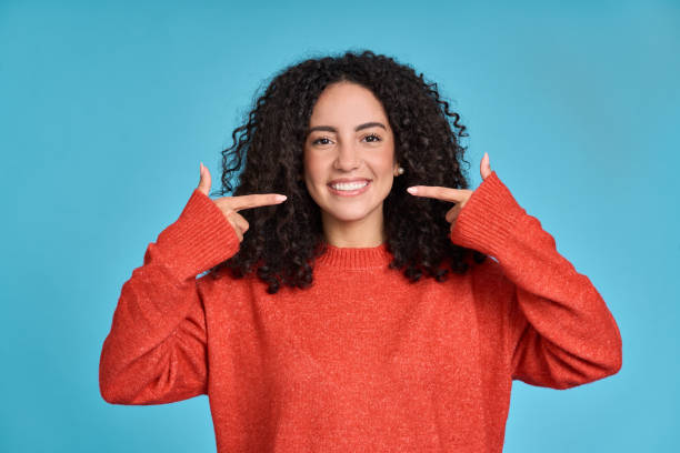 a woman smiling widely while pointing to her beautiful, healthy teeth